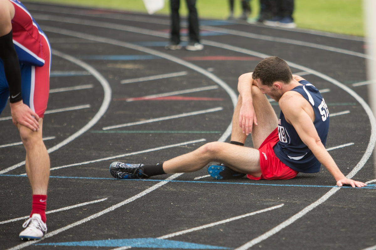 Athlete sitting on a track with another athlete running past